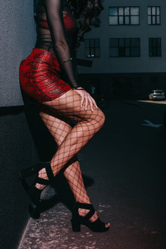 cropped view of prostitute in red skirt and mesh stockings standing near wall