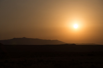 Morning landscape with mountains and orange sky at sunrise with sun reflecting. Evening sunset on the horizon of hills