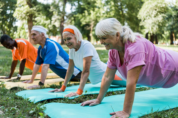 Fototapeta na wymiar selective focus of happy senior woman doing plank exercise with multicultural pensioners on fitness mats