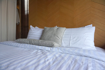 Fototapeta na wymiar White pillows and light grey throw pillow on the white bed sheet with timber backdrop