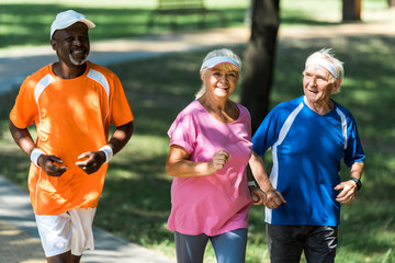 selective focus of happy retired woman running with multicultural men