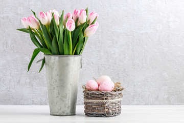 Bouquet of white tulips in ceramic vase and basket of Easter eggs on the table