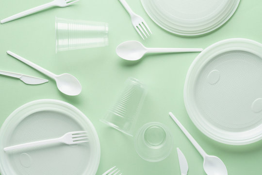 Various white plastic disposable tableware on green background.