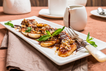 Grilled banana with walnut and chocolate sauce on white plate over brown background