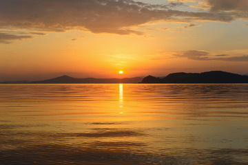 Beautiful cloudy sunset and sea landscape. Gold colored sky and sea, hills silhouette in the evening.