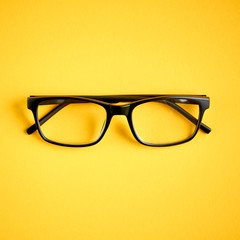 Black glasses on yellow background composition, eyeglasses.