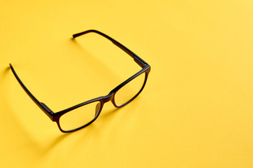Black glasses on yellow background composition, eyeglasses.