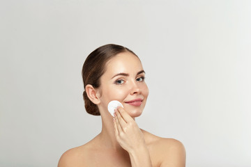 Healthy fresh girl removing makeup from her face with cotton pad. Beauty woman cleaning her face with cotton swab pad isolated on grey background. Skin care and beauty concept. © verona_studio