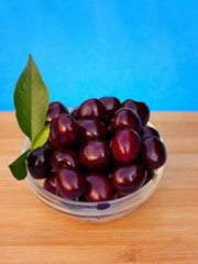 Fruits. A cup of dark red sweet sweet cherries with green leaves on wooden delivery against a blue background.