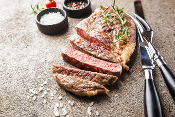 Sliced medium rare grilled beef steak with rosemary and spices on dark rustic background, top view, place for text