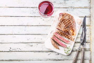 Sliced medium rare grilled beef steak on rustic cutting board with rosemary and spices , white...
