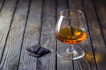 Glasse of brandy or cognac and chocolate on dark background.