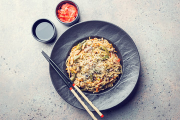 Plate of wok or stir fry noodles with meat and vegetables over gray stone background, top view