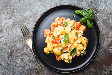 Homemade italian gnocchi with tomato, garlic, basil and mozzarella cheese on stone background. Top view. Copy space.