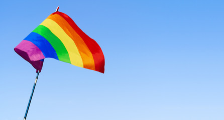 Gay rainbow flag waving in the wind in a clear blue sky