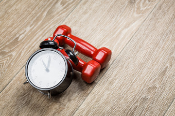 Time for exercising concept. Clock and dumbbell