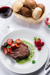 beef stake with strawberry on white dish and basil saus