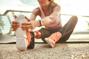 Stretching exercises. Cropped photo of young beautiful woman in headphones with leg prosthesis...