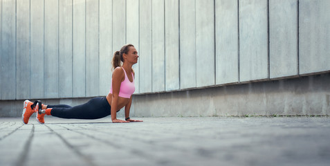 Morning workout. Full-length of young disabled woman with leg prosthesis in sportswear doing stretching exercises outdoors.