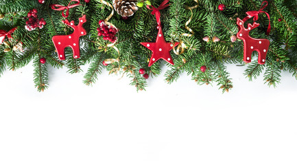 Fototapeta na wymiar Festive Christmas border, isolated on white background. Fir green branches are decorated with red stars, berries, fir cones and red toy deer, close-up, copy space.