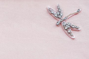 Dragonfly brooch from rhinestones and beads on pink fabric background with copy space. Embroidered...