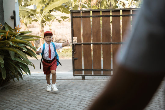 asian elementary student wearing school uniform running toward his parent coming from school