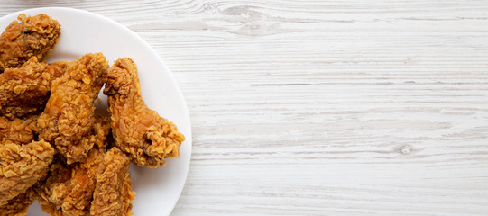 Chicken wings on a round white plate on a white wooden background. Overhead, flat lay, from above....
