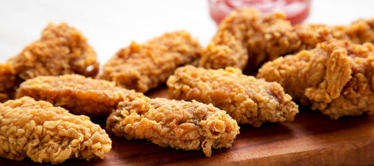 Chicken wings on a rustic wooden board with red pepper sauce on a white wooden background, side view. Close-up.