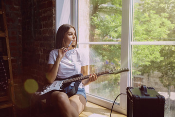 Woman in headphones recording music video blog home lesson, playing guitar or making broadcast internet tutorial while sitting in loft workplace or at home. Concept of hobby, music, art and creation.