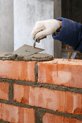 Hand with a trowel, in the process of laying a wall of red brick.