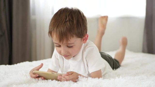 Cute little boy playing using smartphone. The child looks at the smartphone screen and laughs. Applications for the development of children.