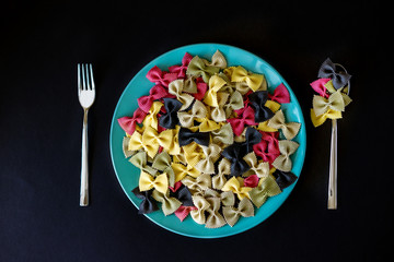Multicolor italian raw pasta close up in a ceramic plate with metal fork and spoon isolated on the...