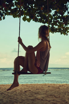 Young woman swinging on a sandy tropical beach.