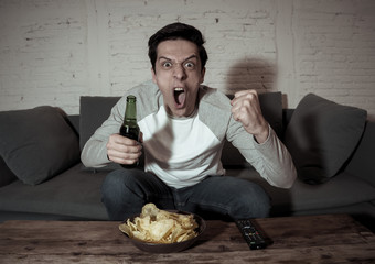 Excited young sports fan man watching soccer game on television ,celebrating goal and screaming
