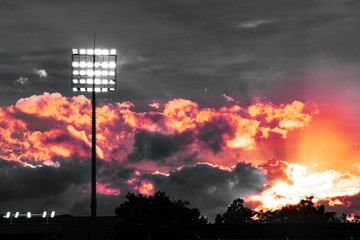 white light electric pole at sport stadium with dramatically sky and red orange light evening sky