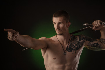 muscular guy with bare torso posing on a dark background with a sword