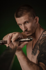 muscular guy with bare torso posing on a dark background with a sword