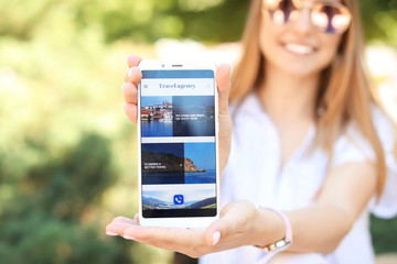 Woman holding mobile phone with open page of travel agency website