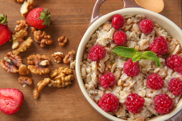 Pot with tasty sweet oatmeal, berries and walnut on table