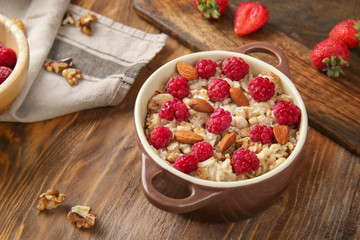 Pot with tasty sweet oatmeal, raspberry and almond on wooden table