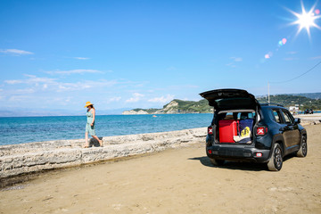 A woman in a hat and sunglasses and a car on a sunny sandy beach