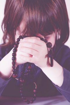 Little child girl praying and holding a wooden rosary