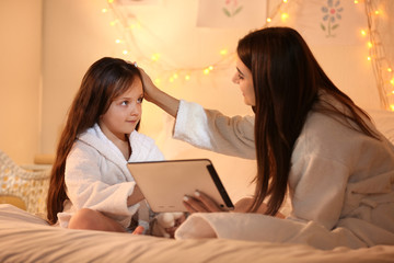 Woman and her cute little daughter with tablet computer in bedroom