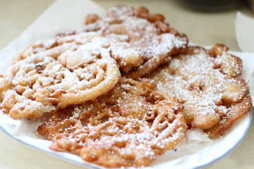 Homemade funnel cakes with powdered sugar on a ceramic plate.