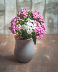 A bouquet of wild carnations in a grey clay vase on a wooden table