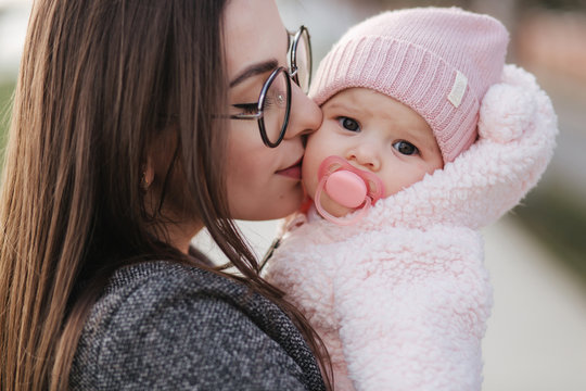 Portrait of mother and her little baby girl. Beautiful mom and cute baby. Mother hud her daughter. Baby dressed in peanch colour hat and nipple toy