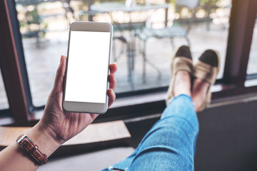 Mockup image of a woman holding white mobile phone with blank desktop screen while sitting in cafe
