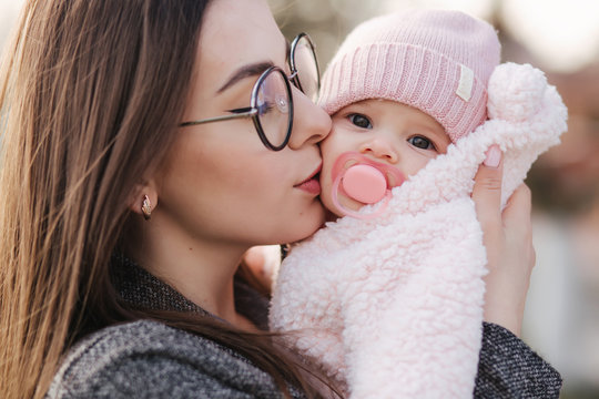 Portrait of mother and her little baby girl. Beautiful mom and cute baby. Mother hud her daughter. Baby dressed in peanch colour hat and nipple toy