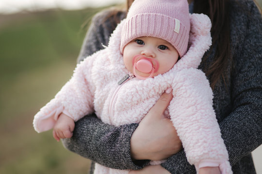 Little baby girl on mother's hands in pink clothes. Cute baby with peanch colour nipple toy