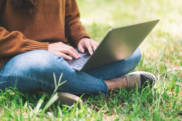 Closeup image of a woman working and typing on laptop keyboard while sitting in the outdoors